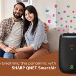 A young couple sitting on the couch with SHARP QNET SmartAir air purifier in the frame