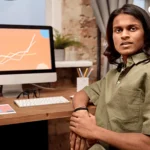 A-man-sitting-in-front-of-his-computer-with-a-sales-graph-going-upwards-on-the-screen