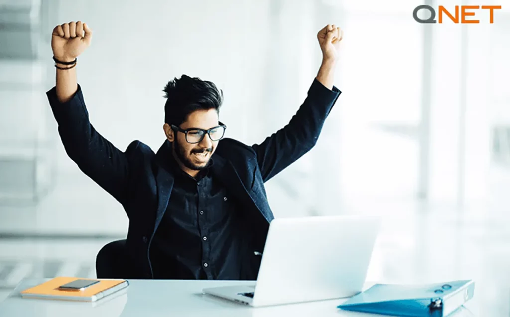 A young Indian business man in a suit celebrating in front of his laptop.